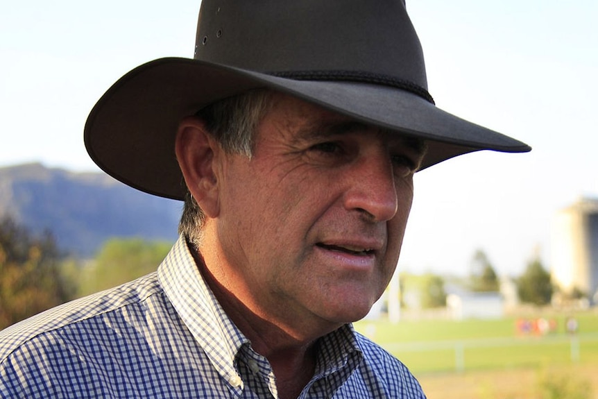 John Anderson, wearing an Akubra hat and checked shirt, stands on a farm
