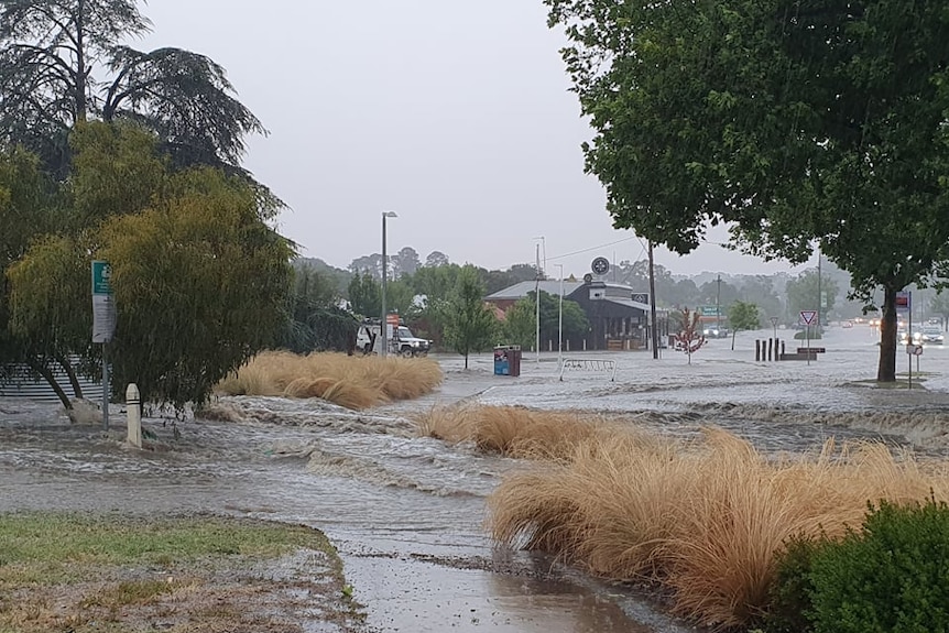 a road and footpath are covered by rain which is rushing fast and looks like river rapids.