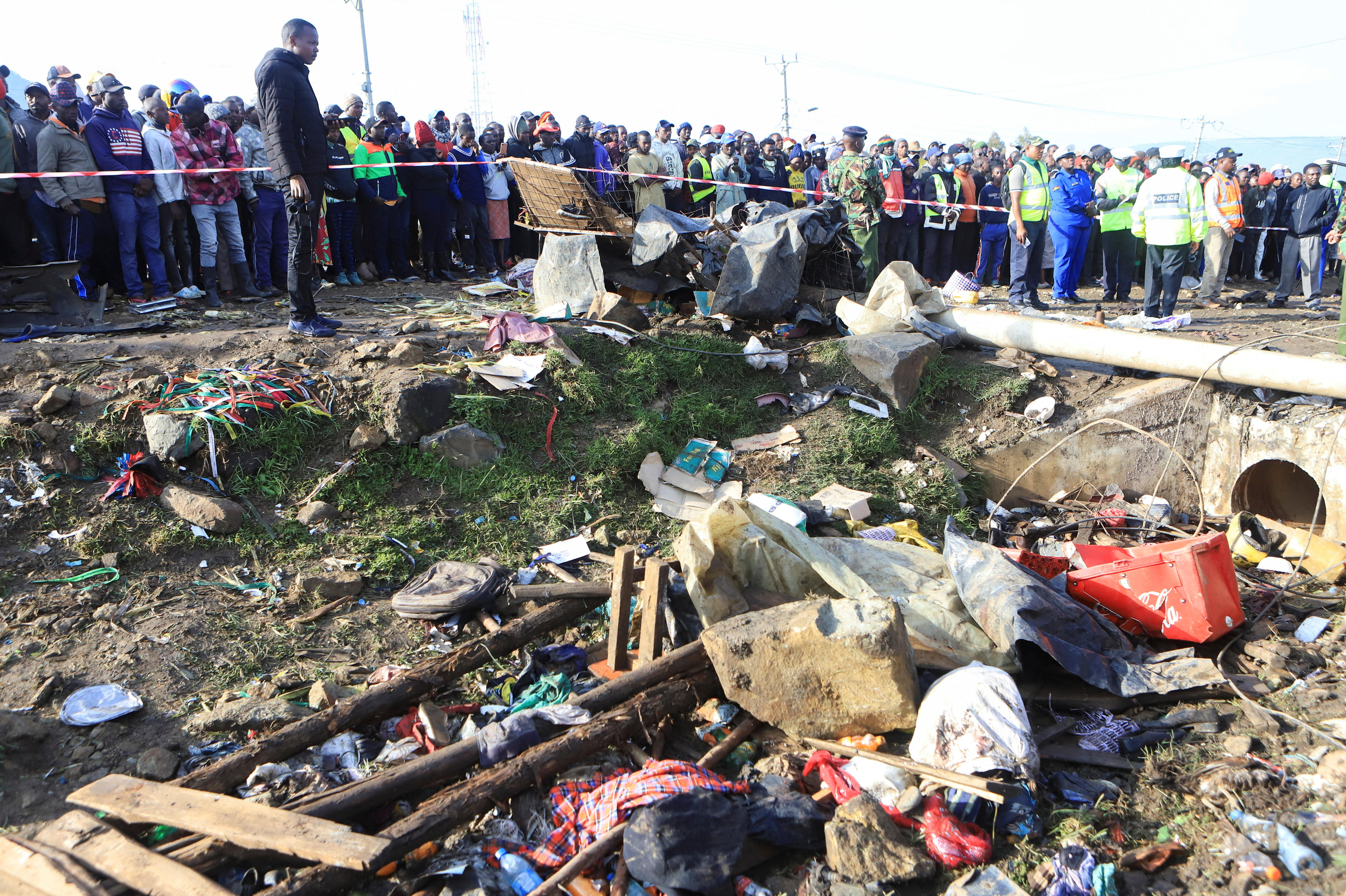 A view of debris and damaged items with people looking on in the background.