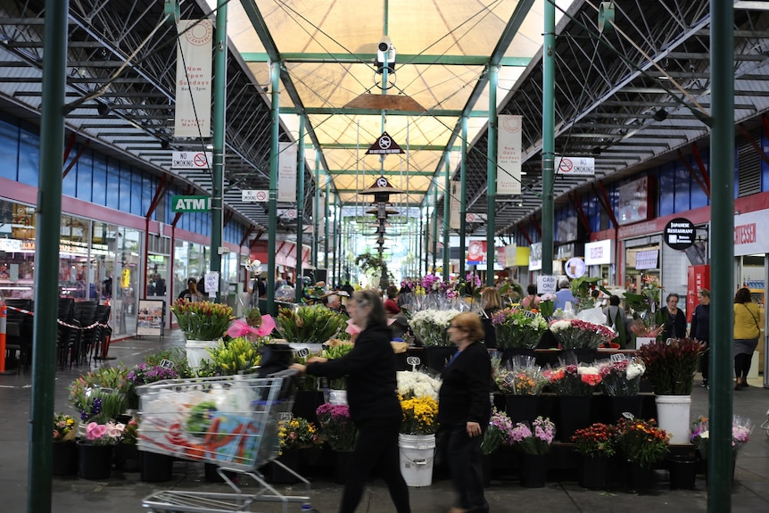 Two women walk past a florist under the high, airy frames of the Preston Market.