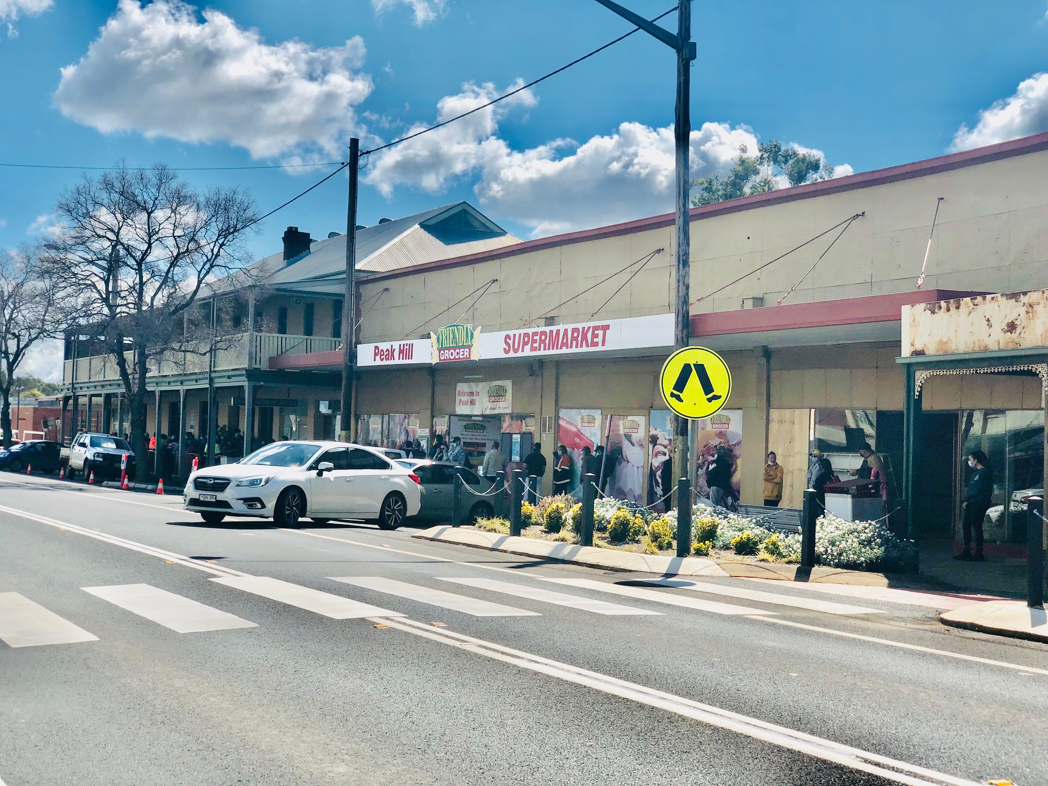 A long line of people wearing face masks stretches past a supermarket.