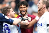 Tyrone Mings smiles while touching the face of Pontus Jansson. Two more Leeds players approach Mings and prepare to grab him.