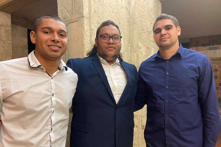 Three men in formal wear smile outside a courthouse