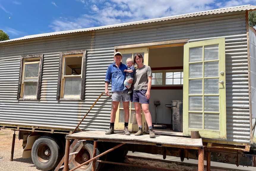 A young family stands at the entrance to a demountable-style building.