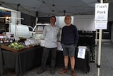 A farmer and worker stand in front of their stall at the farmers' markets.