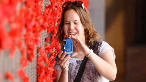Teenage girl takes a photo beside memorial wall full of poppies at Australian War Memorial
