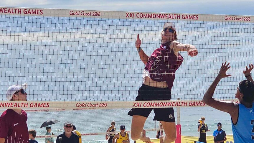 A young boy clad in maroon tee rises above the net for a spike at the national beach volleyball titles