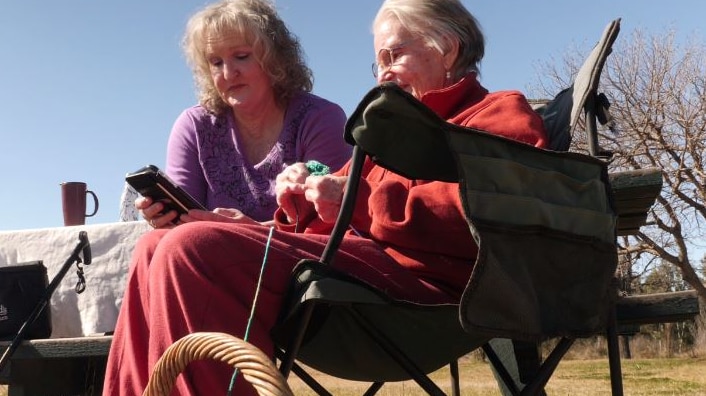Two ladies in a park knitting.