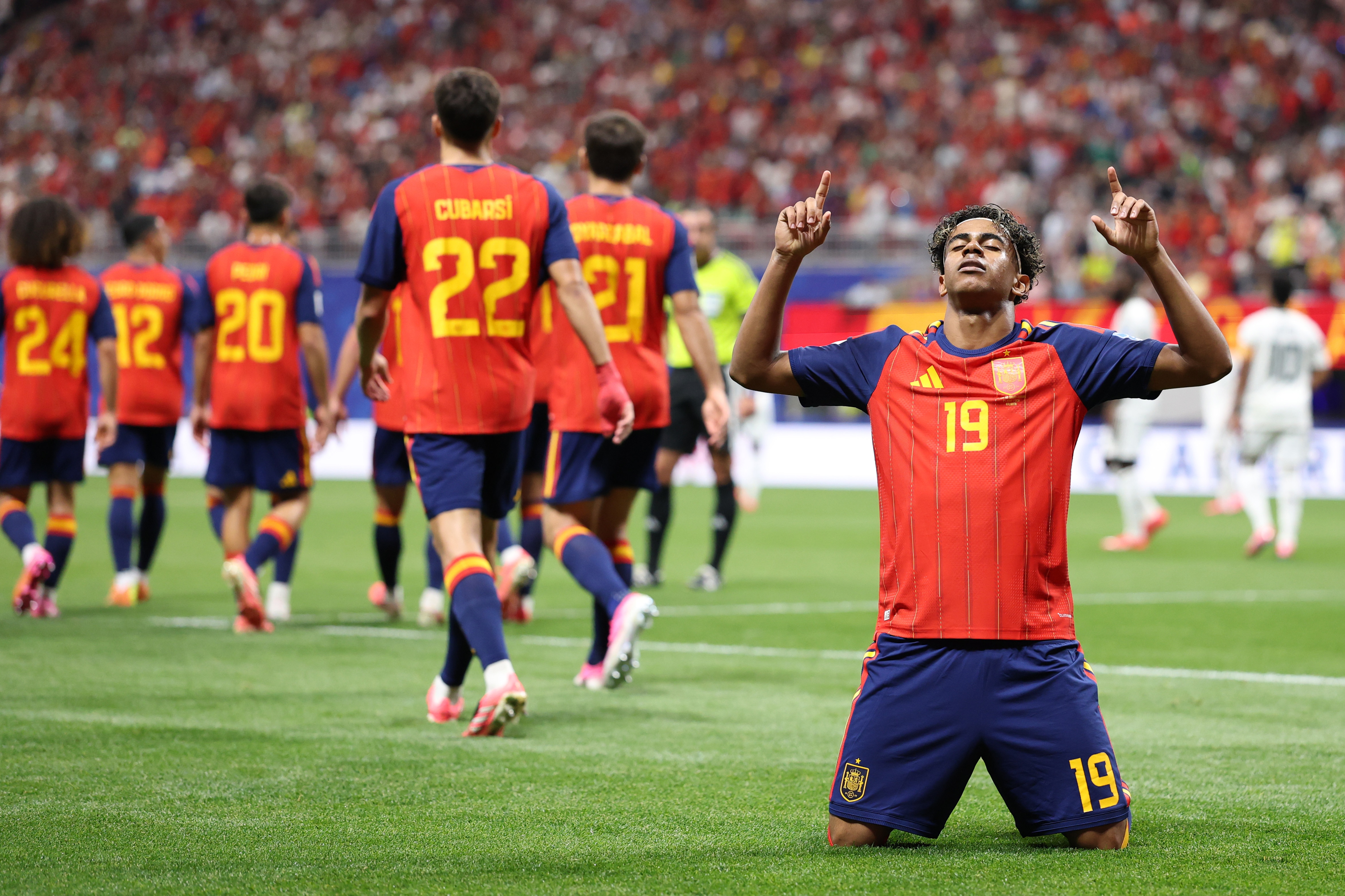 Lamine Yamal points to the sky in celebration while on the soccer field. 