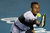 Tennis player stretches his racquet out to hit a backhand return.