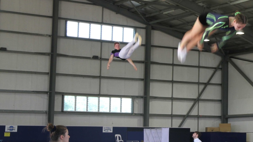 Two people bouncing on a trampoling in an indoor stadium