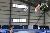 Two people bouncing on a trampoling in an indoor stadium