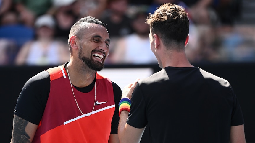 Two Australian male tennis players share a laugh on court during the match.