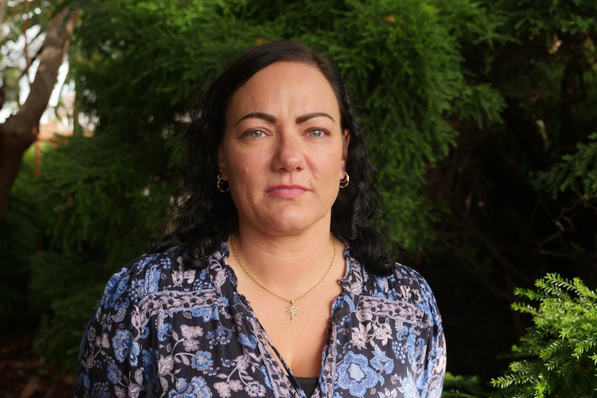 A close up of a woman with short dark hair staring down the barrel of the camera. She's wearing a dark patterned top