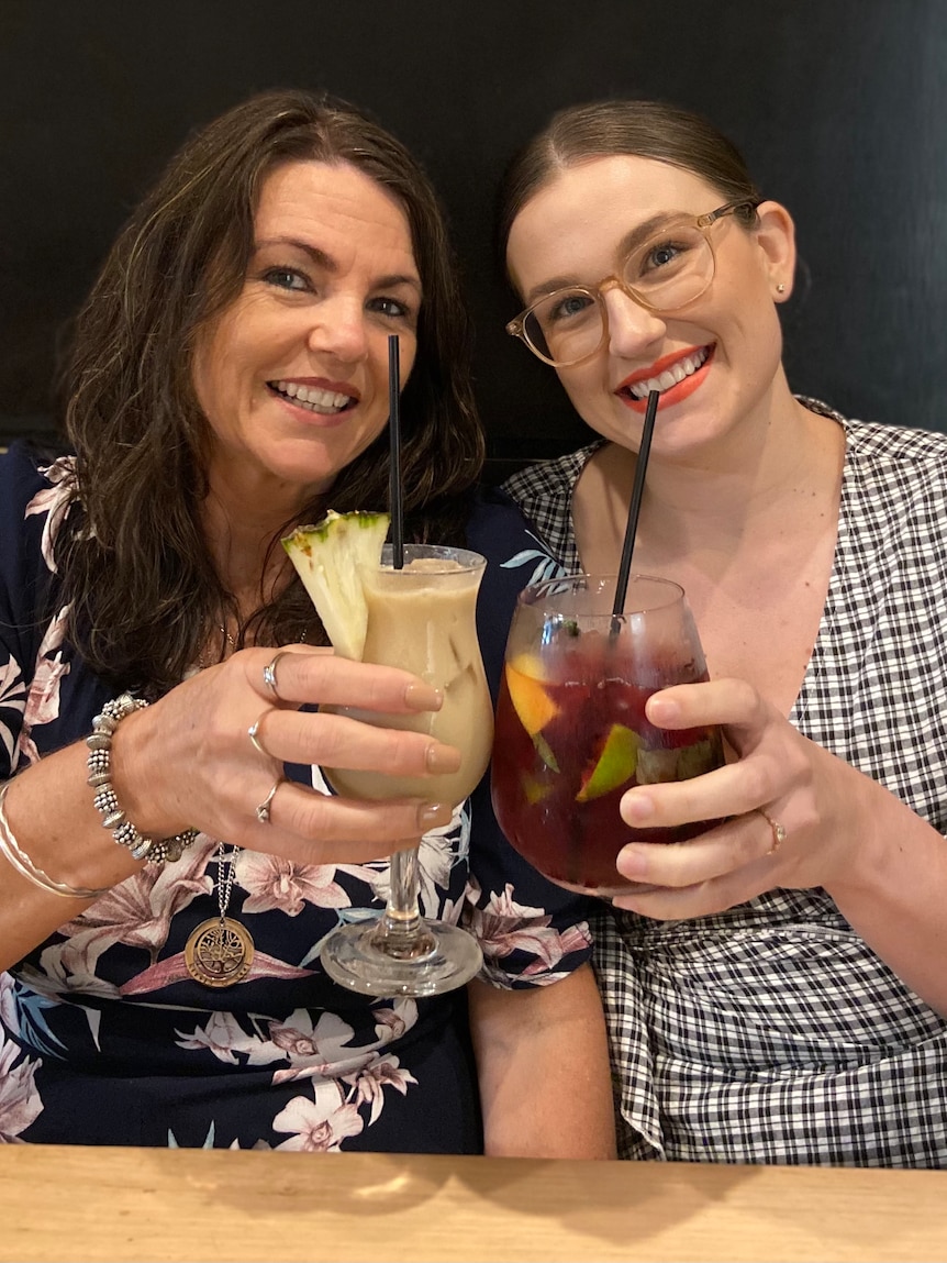 Two women sitting at a table smiling and clinking their glasses together.