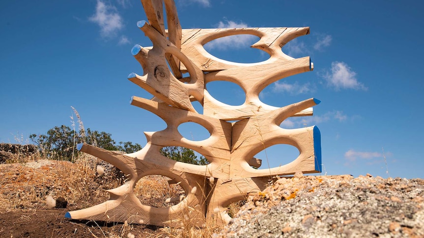 A wooden sculpture with ovals carved out of it sits on a hillside.