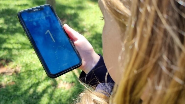 A young girl with blonde hair holds a phone with a cough screening app in a garden