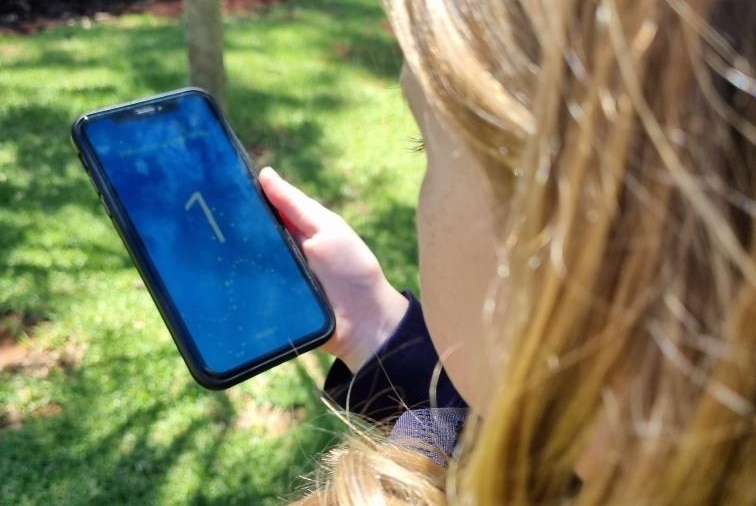 A young girl with blonde hair holds a phone with a cough screening app in a garden