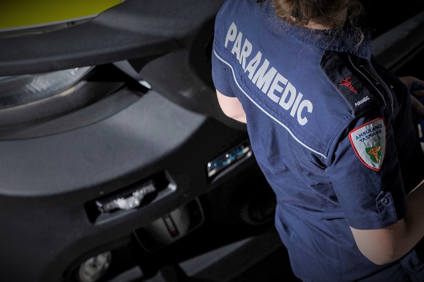 Unidentified female Ambulance Tasmania paramedic walks past an ambulance.
