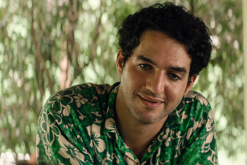 30-годишен мъж в зелена хавайска риза се усмихва леко, с тъжно изражение