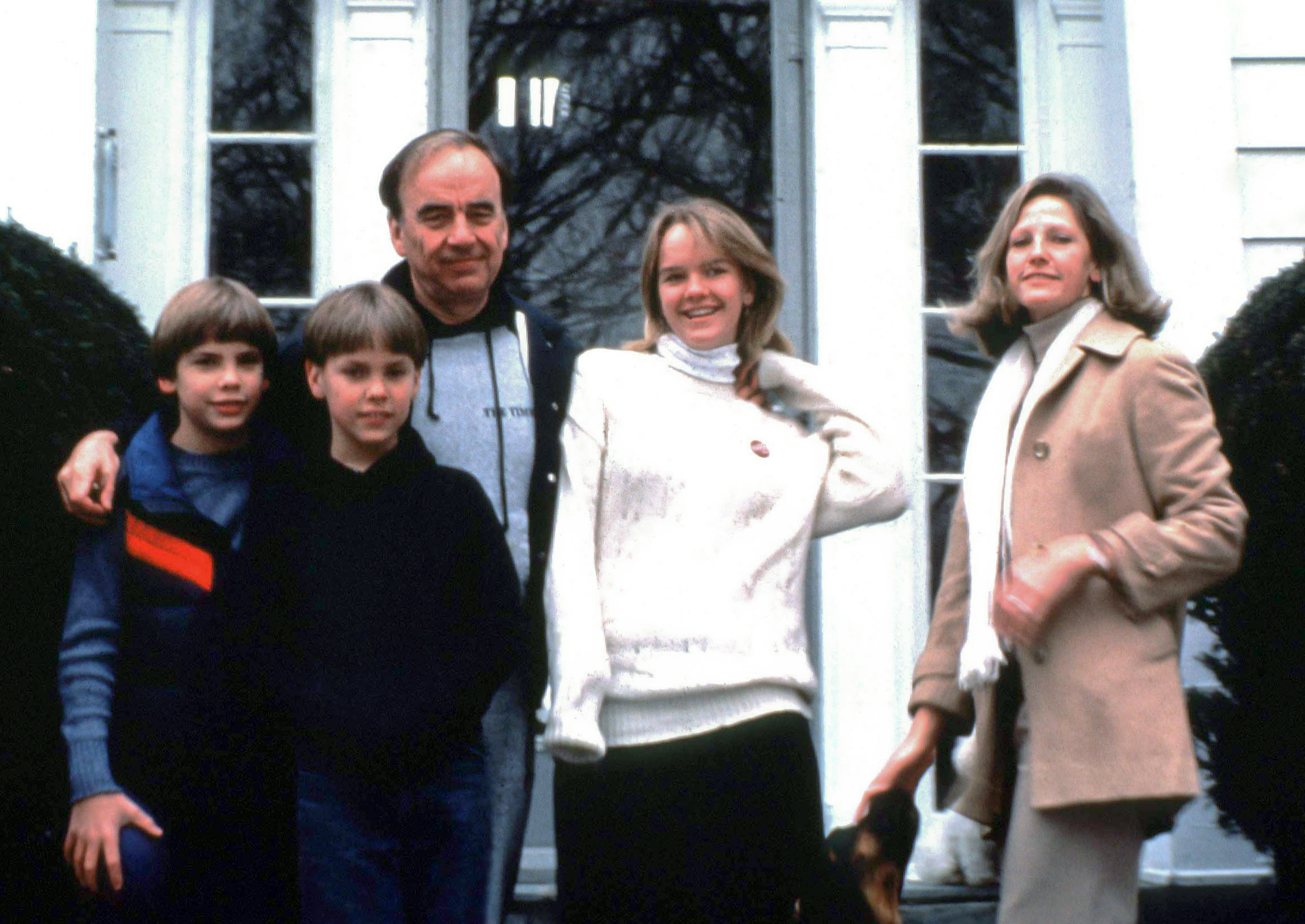 A man, a woman, and three teens pose together outside a house