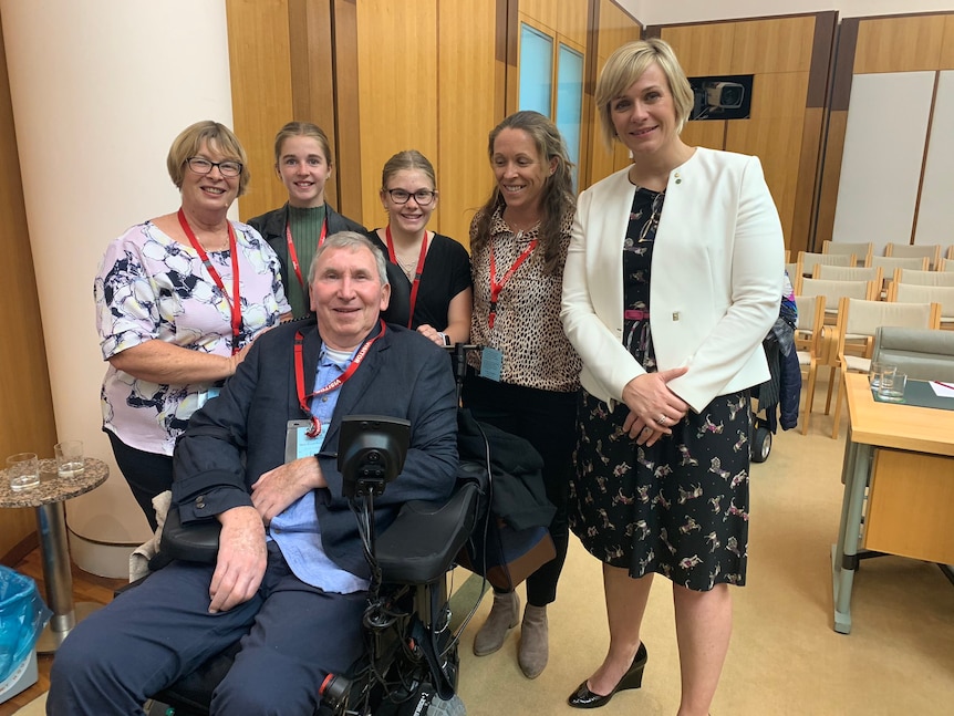 Five women stand behind a man in a wheelchair.