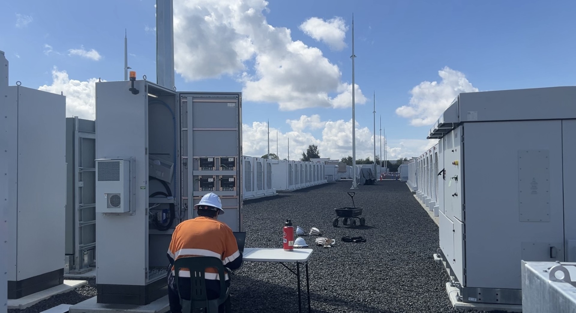 A worker in high-vis sits in front of a grid-scale battery.