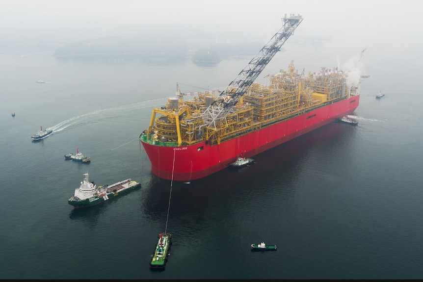 A 488 metre long floating liquified natural gas facility in the ocean with some smaller vessels around it.