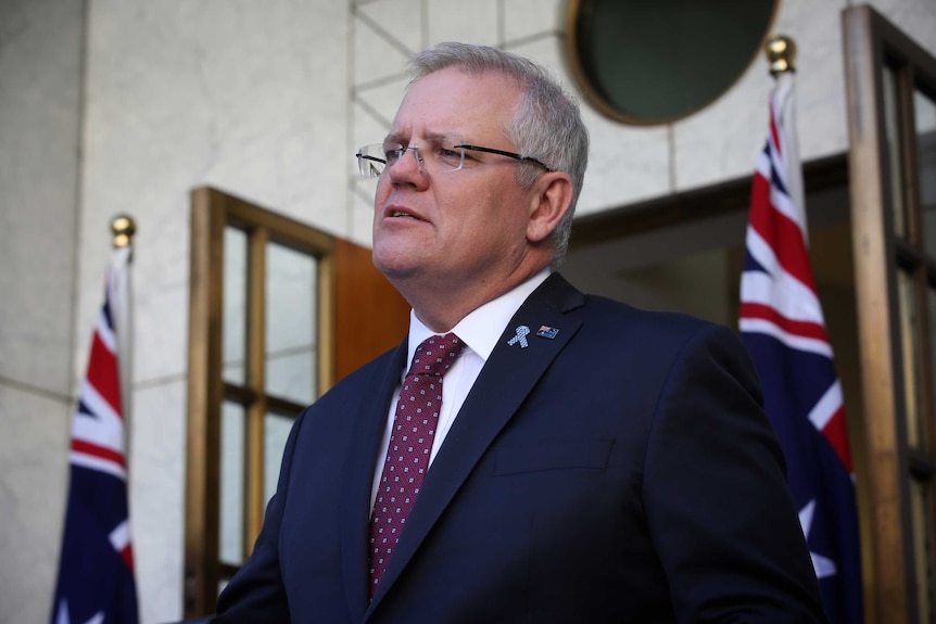 Prime Minister Scott Morrison at a press conference outside, there are two Australian flags behind him