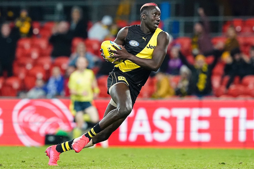 A Richmond Tigers AFL player runs with the ball in two hands during a match against North Melbourne.