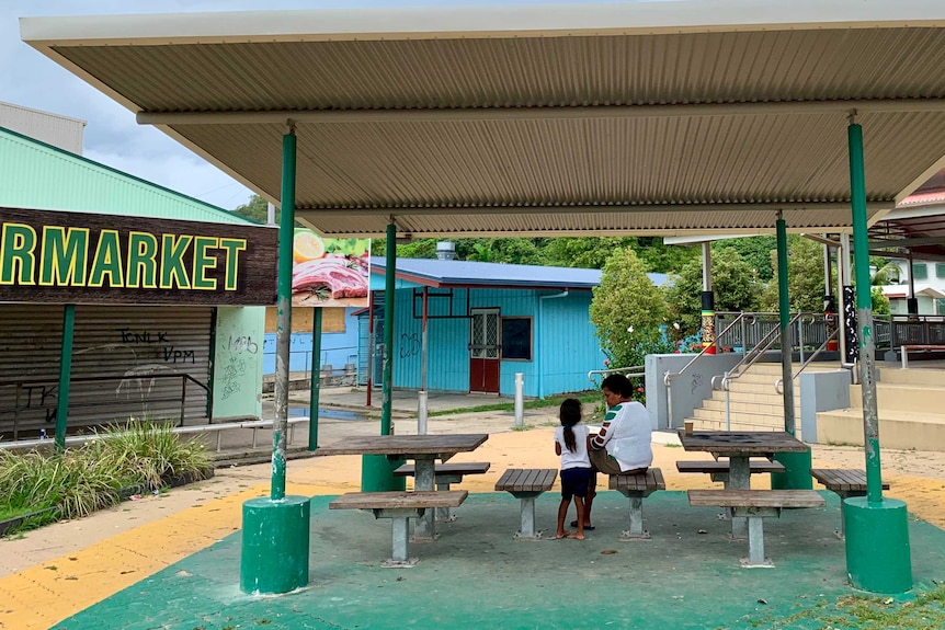 A woman and child sitting on table and chairs out the front of the grocery shop on Palm Island Jan 2020