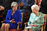 Queen Elizabeth II and Theresa May sit next to each other at the opening ceremony. May is clapping and looking at the queen.