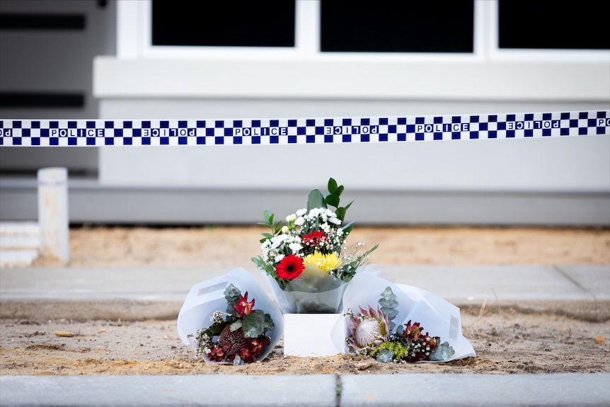 Flowers sit on a street verge with police tape lined above