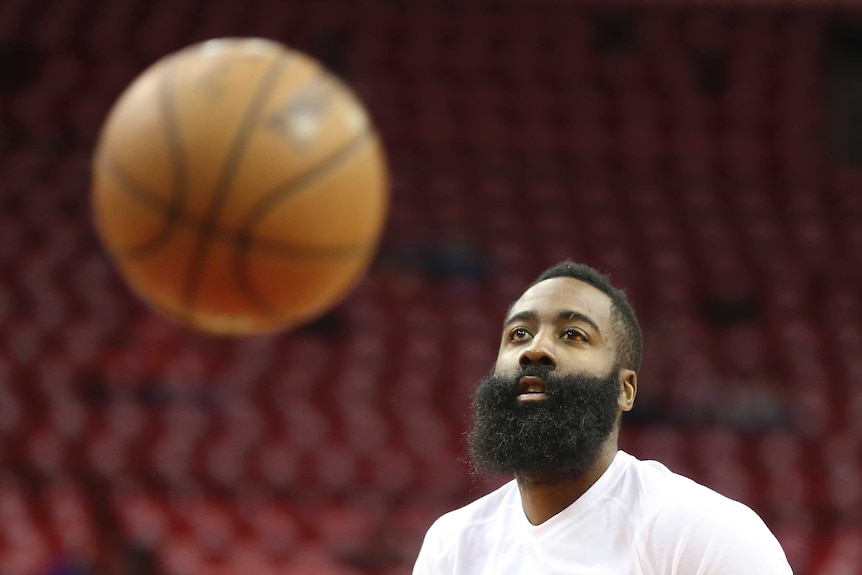 James Harden wearing a white shirt with a basketball in front of him.