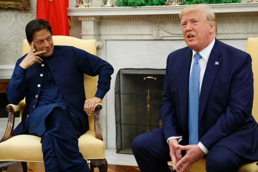 Imran Khan holds his hand up to his face while watching Donald Trump speak at the White House.