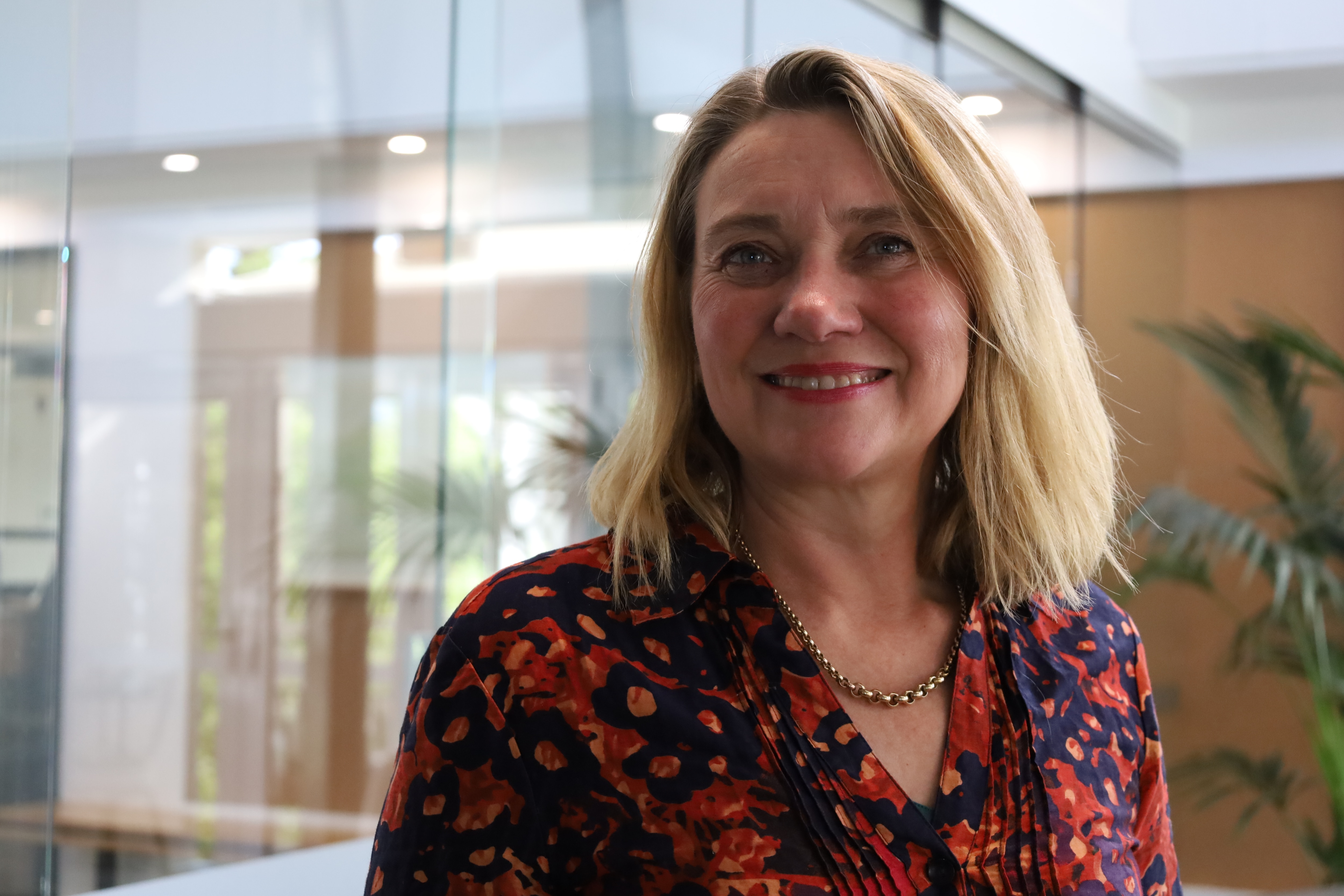Josie Kelman wears a navy and orange blouse and a gold necklace and smiles at the camera.