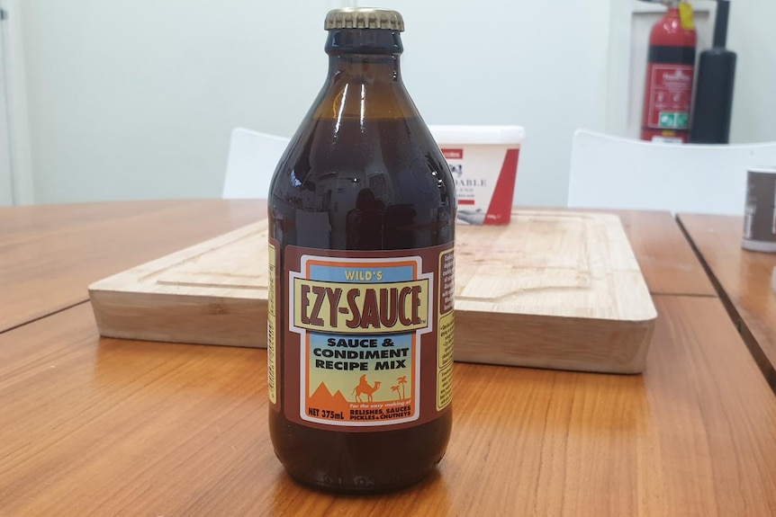 A brown glass beer bottle with the words "Wid's Ezy sauce' on its label rests on a wooden table.
