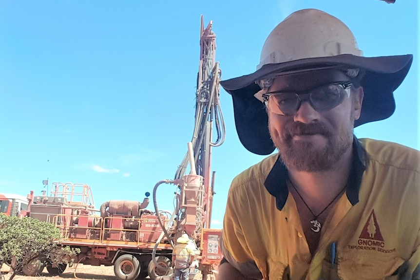 Richard wears a hard hat, safety glasses and high vis on an exploration site