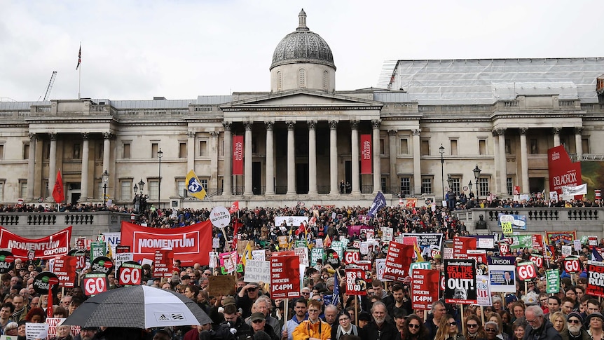 Trafalgar Square is filled with protesters holding banners on various issues.