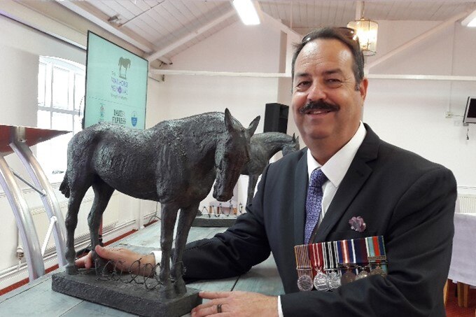 A man wearing war medals holds a small statue of a horse.