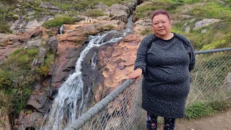 A middle-aged woman stands in front of a waterfall.
