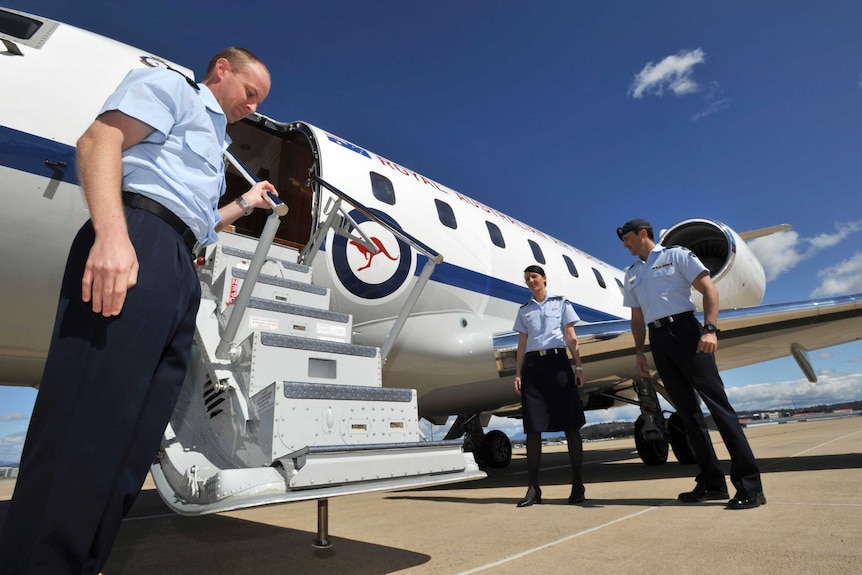 Three people in uniform stand next to stairs of a small jet.