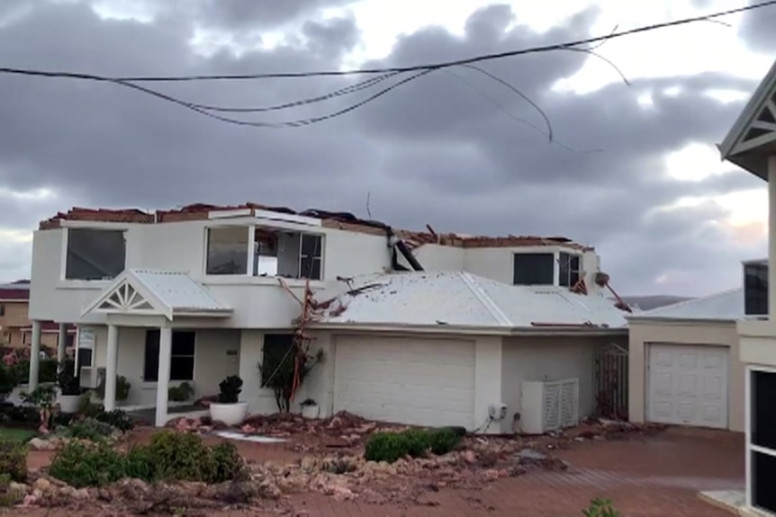 A large two-storey house is missing its entire roof. There is debris in the garden.