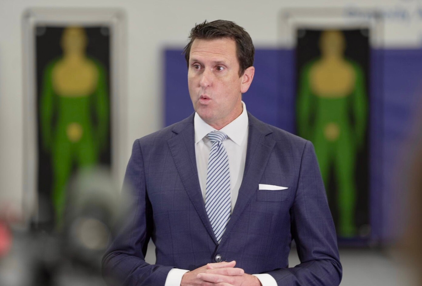 Un hombre de traje habla frente a dos objetivos con forma humana.