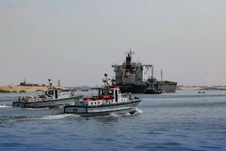 Two tug boats headed towards a bulk carrier ship. 