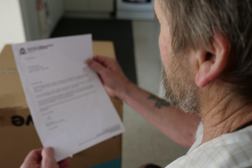 A man holds an official letter in front of moving boxes.