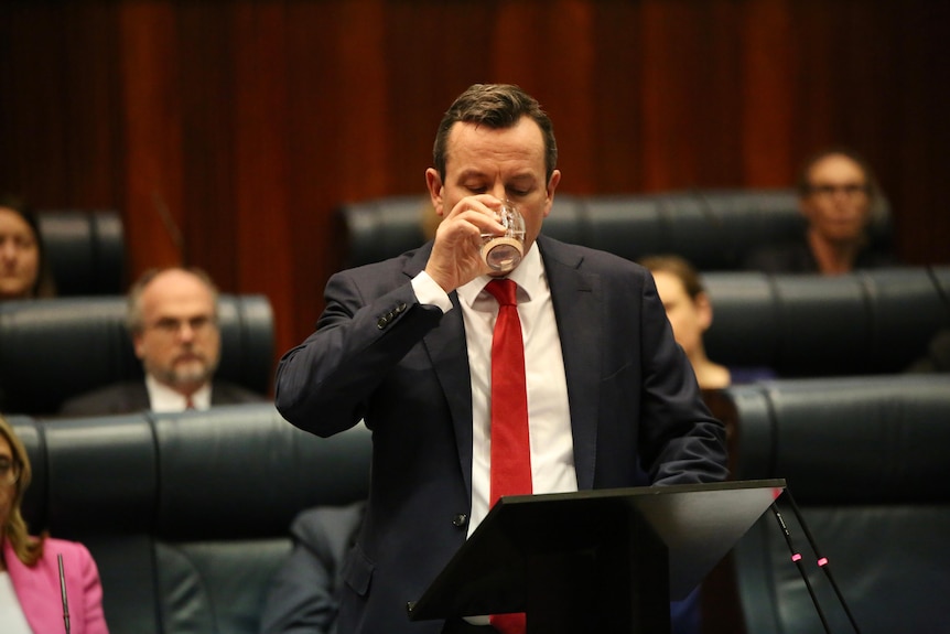 A photo of Mark McGowan drinking a glass of water in parliament.