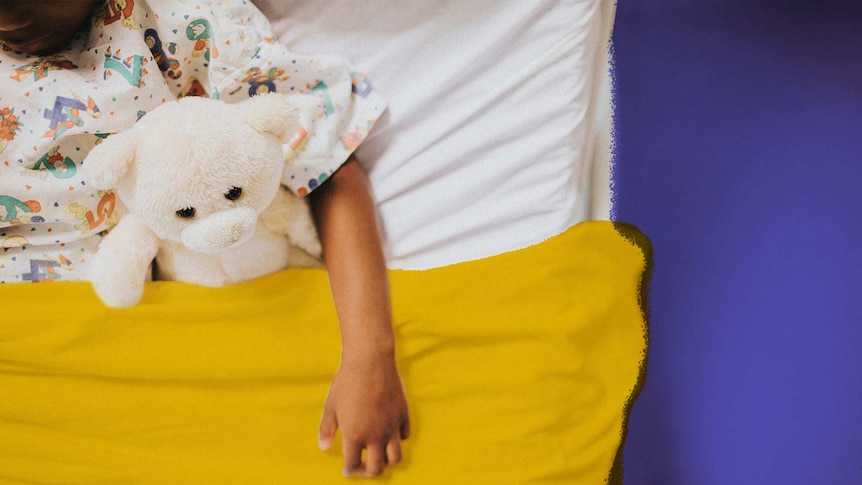 A young child sits in a hospital bed with a teddy bear.