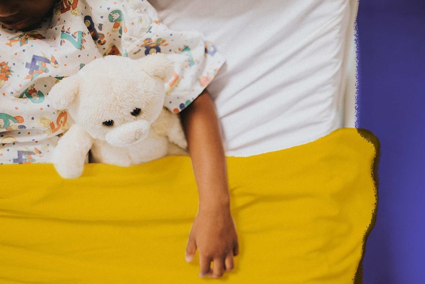 A young child sits in a hospital bed with a teddy bear.