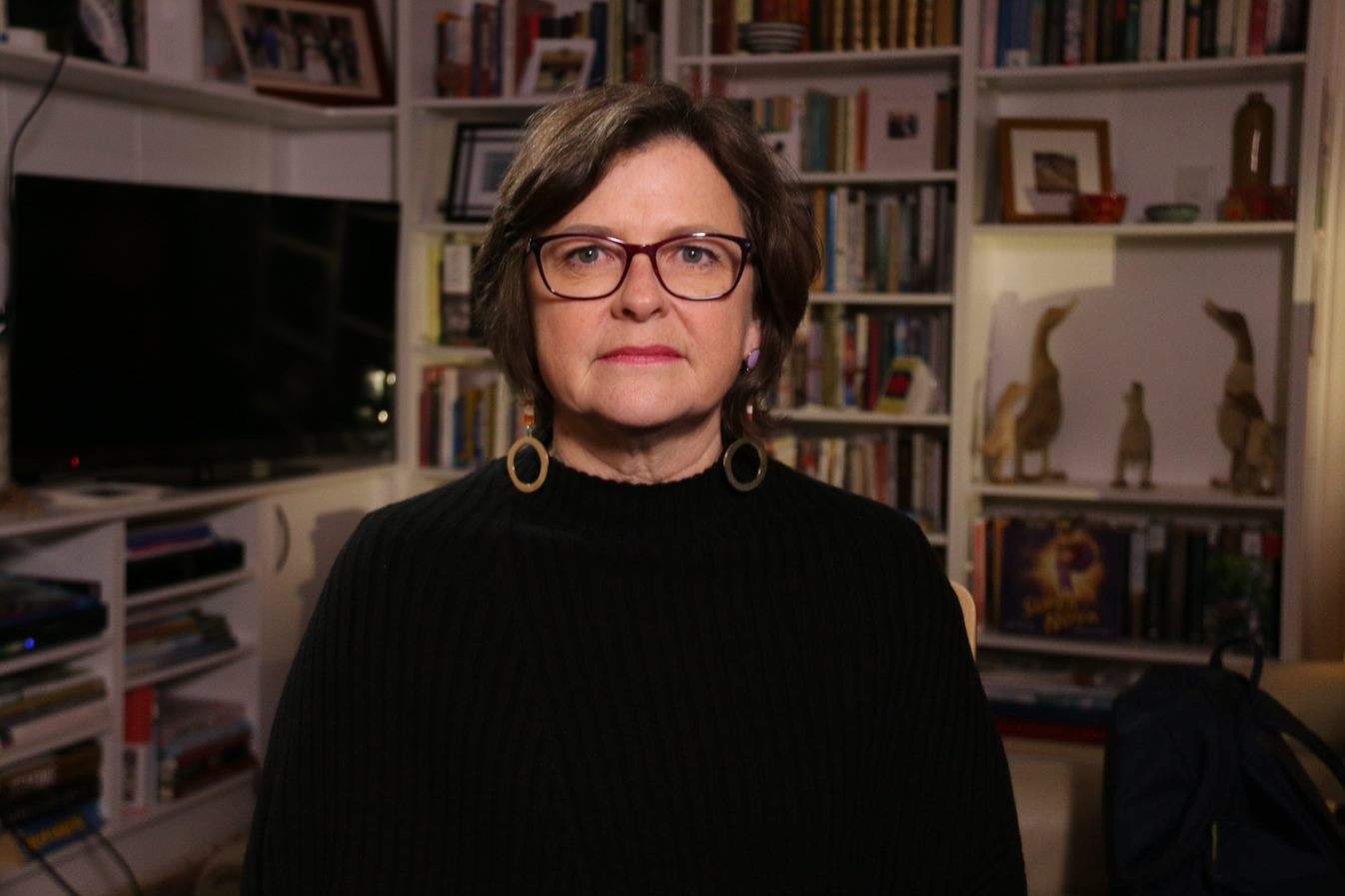 A woman wearing glasses with a bookcase behind her.